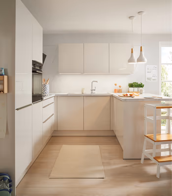 Moderne weiße Küche mit grifflosen Fronten, U förmigem Grundriss, heller Arbeitsplatte und Holzfußboden. Pendelleuchten, integrierte Elektrogeräte und viel Tageslicht schaffen eine freundliche und funktionale Küchenlösung.